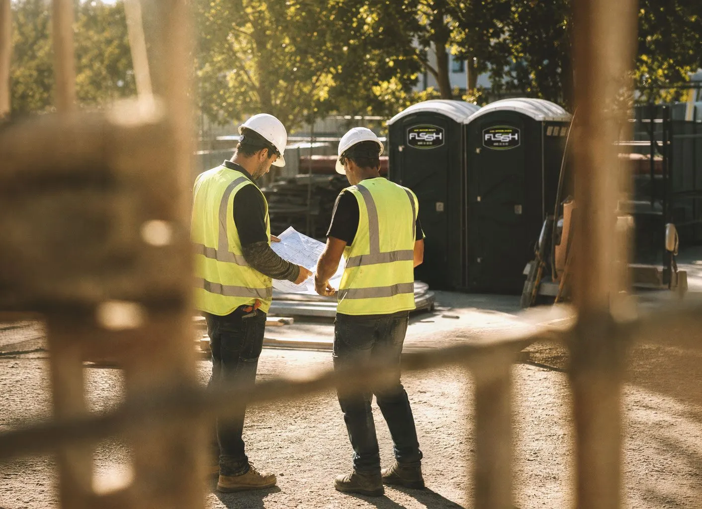 Construction crew reviewing plans in front of a row of FLSSH portable toilets