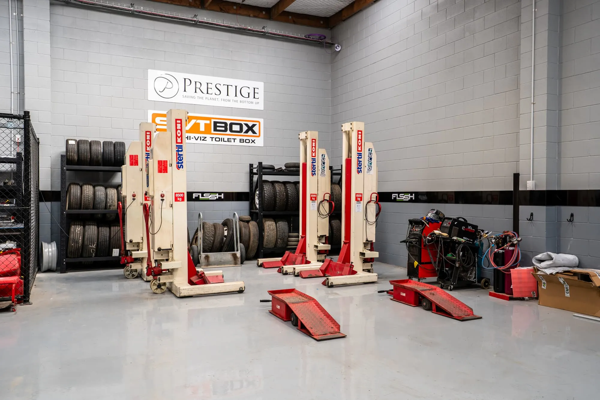 Truck hoists and tyre racks in the FLSSH workshop, under Prestige and SHVTBOX signs
