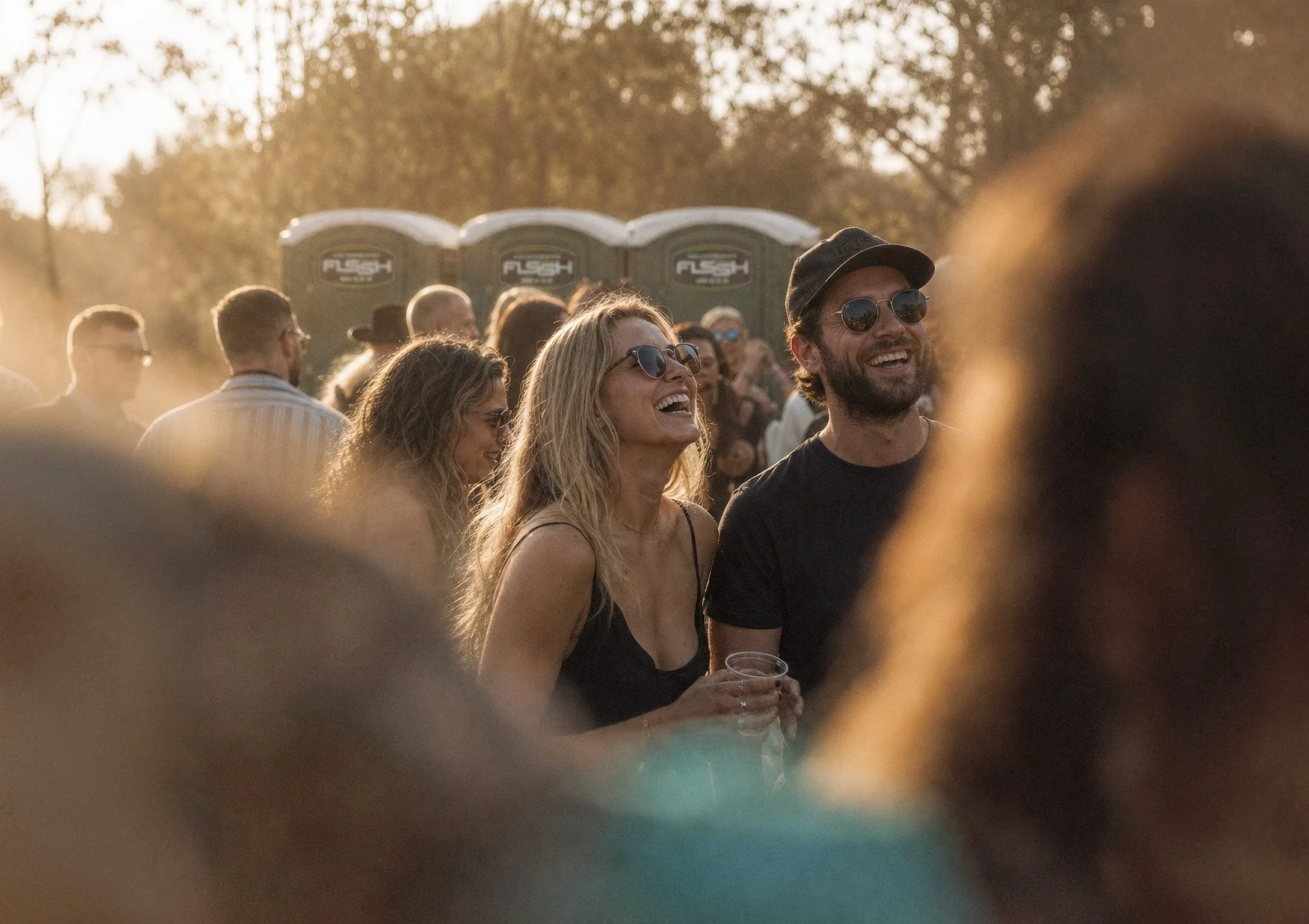 Festival crowd laughing in the sun with FLSSH portable toilets in the background
